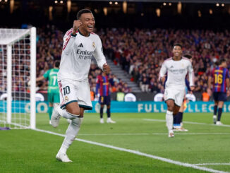 Kylian Mbappé w białej koszulce Realu Madryt celebruje zdobycie bramki podczas El Clásico z FC Barceloną. W tle widoczni są zawodnicy obu drużyn oraz bramka.